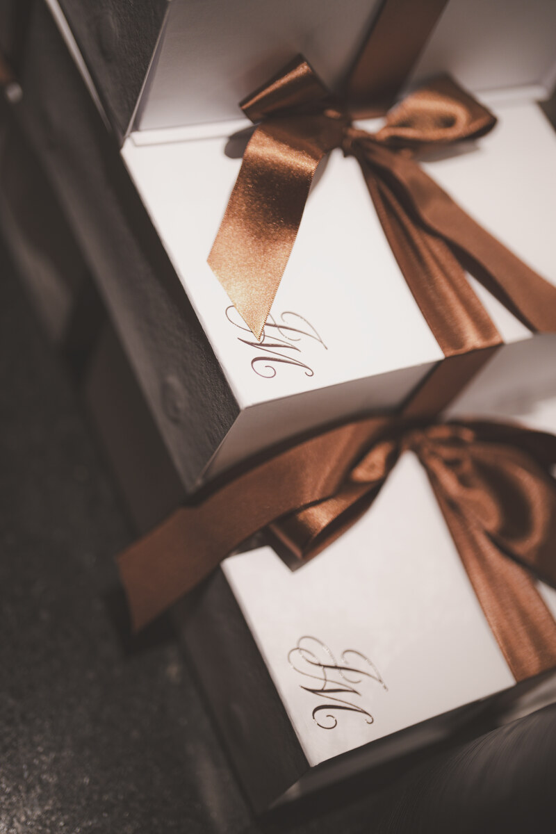 Detalhe dos convites do casamento, com laço de cetim bronze e o monograma de João e Mel.